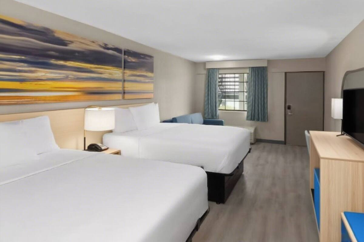 Een hotelkamer met twee bedden, een bureau, een televisie en een schilderij aan de muur.