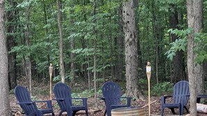 A forested area with four Adirondack chairs arranged around a fire pit. - Charming 3-bedroom with Abundant Outdoor Space (Harrietta)