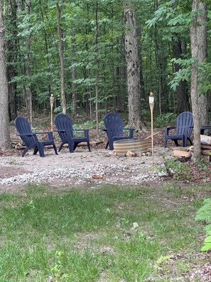 Ein bewaldetes Gebiet mit vier Adirondack-Stühlen, die um eine Feuerstelle angeordnet sind.
