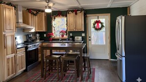 A kitchen with wooden cabinets, a central island with stools, a refrigerator, and a door with a wreath. - Charming 3-bedroom with Abundant Outdoor Space (Harrietta)