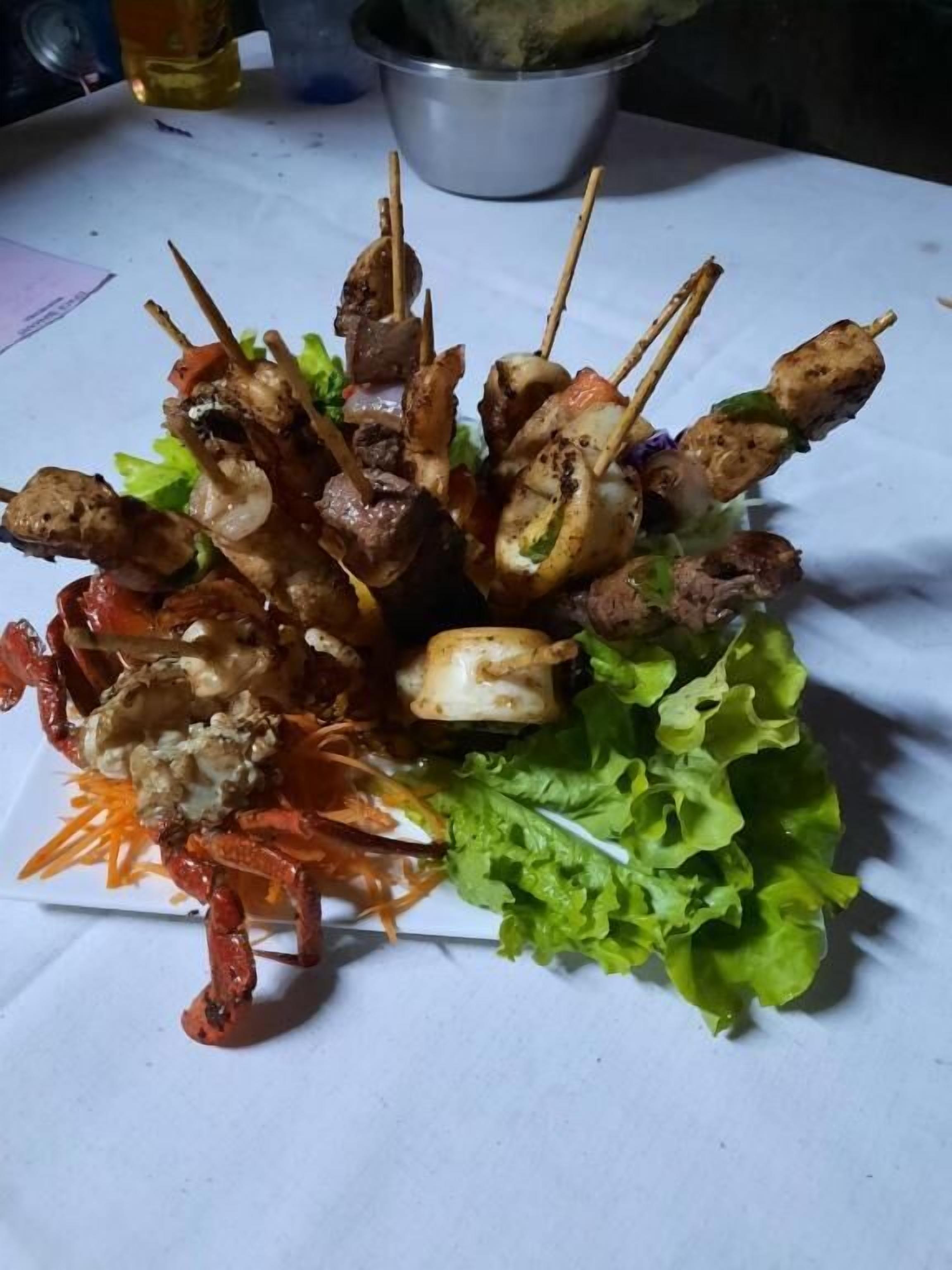 A plate of skewered meats and seafood on a white tablecloth with lettuce.