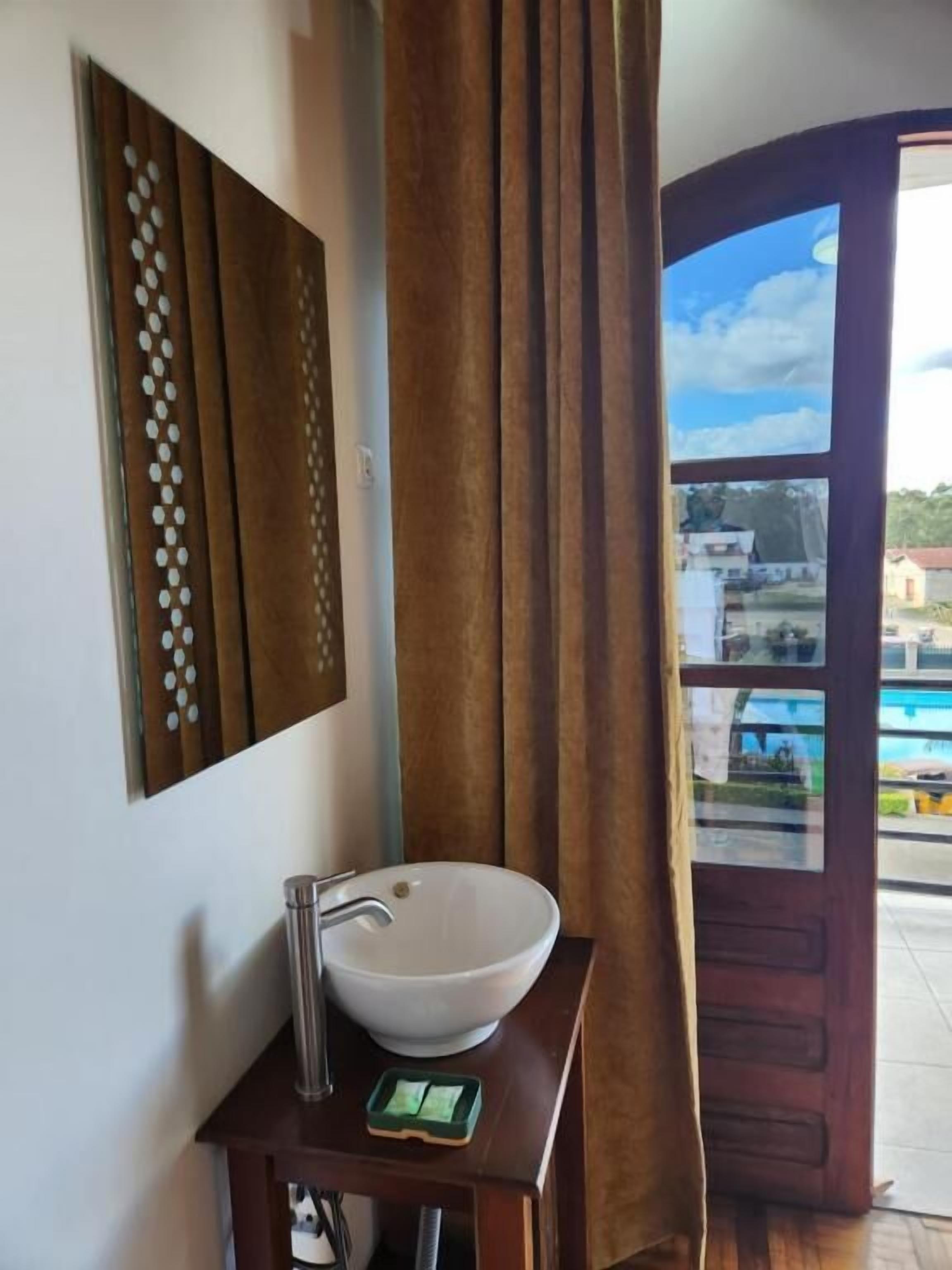 A bathroom with a white sink, a mirror with a decorative frame, and a view of a pool through a glass door.