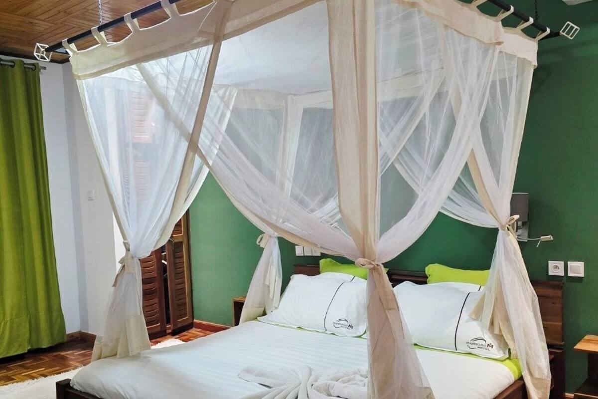 A bed with a canopy, green walls, and a wooden floor.