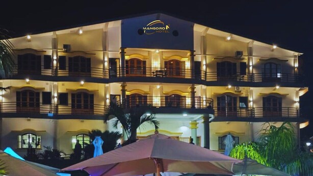 A multi-story hotel with a well-lit outdoor area, featuring tables and chairs under umbrellas, and a pool area. - MANGORO HOTEL (Moramanga)