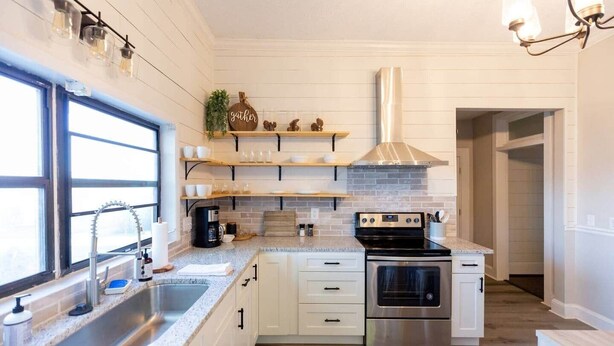 Una cucina moderna con mobili bianchi, piano cottura in acciaio inossidabile e una finestra che offre luce naturale.