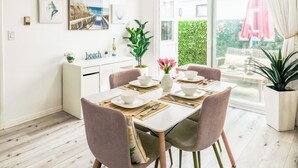 En matplats med ett vitt bord dukat för fyra personer, omgivet av stolar med gröna ben. På bordet står dekorativa skålar och en vas med blommor.