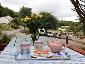 A picnic setup with a table, a vase of yellow flowers, a pink teapot, and cupcakes on a tray. - Bungalow w/pool access @ Honicombe Holiday Village with pool and fitness access (Callington)