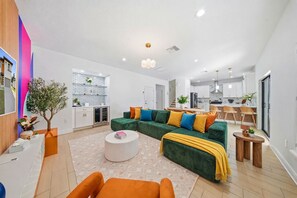 A modern living room with a sectional sofa, a coffee table, and a dining area with wooden chairs. - Tampa Oasis 5 mins from Raymond James Stadium! (Tampa)