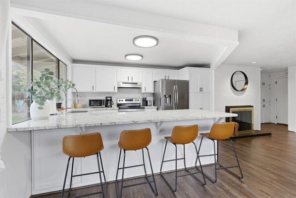 A modern kitchen with white cabinetry, stainless steel appliances, and a marble island with bar stools.