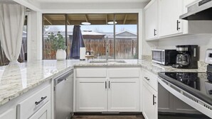 Una cocina moderna con armarios blancos, encimera de granito, estufa, microondas y cafetera.