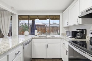 A modern kitchen with white cabinets, a granite countertop, a stove, a microwave, and a coffee maker.