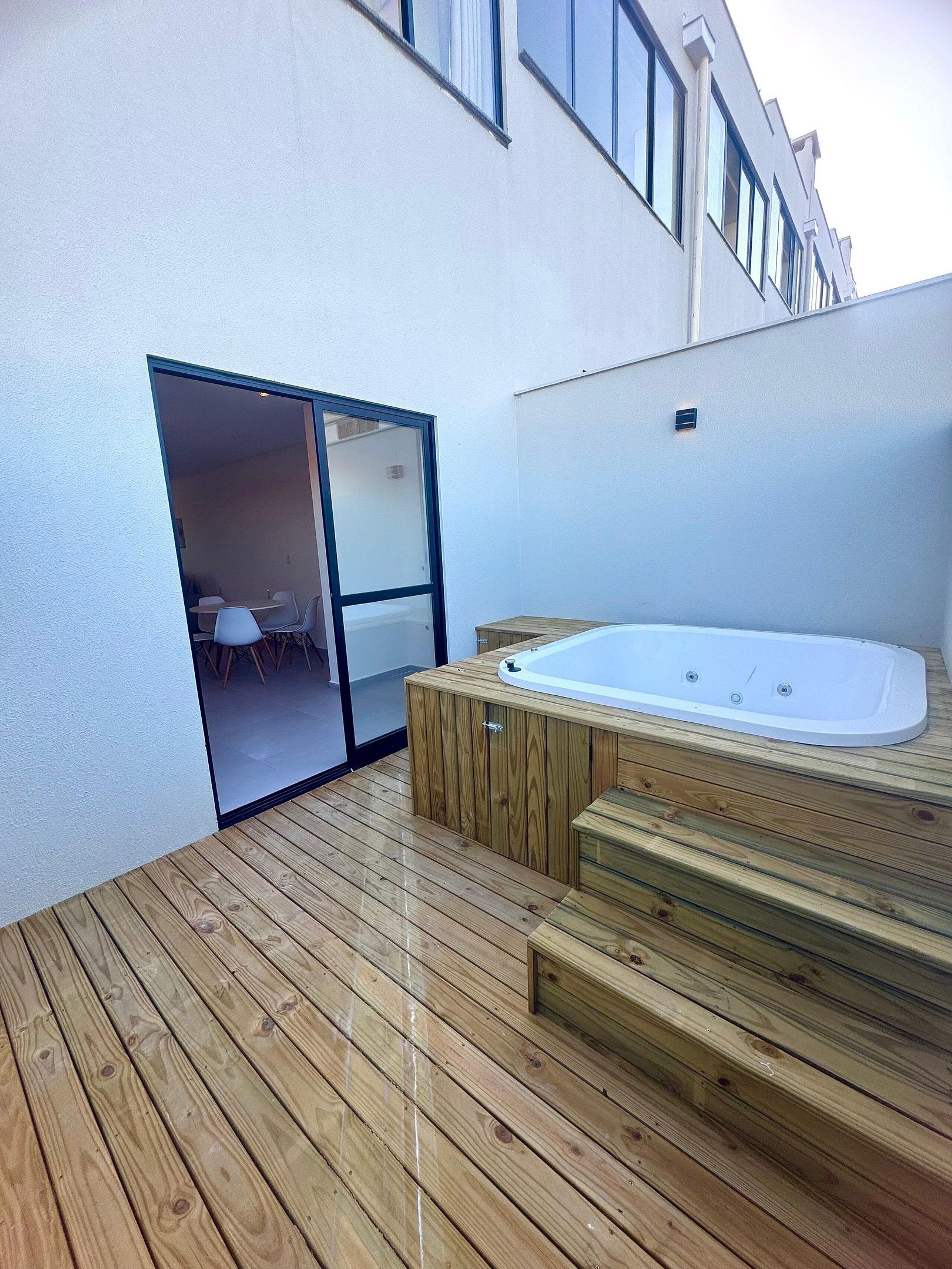 A wooden deck with a hot tub and a sliding glass door leading to an indoor seating area.