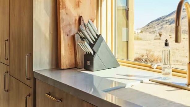 A kitchen with a wooden cutting board, knife block, and a window with a view of a desert landscape.