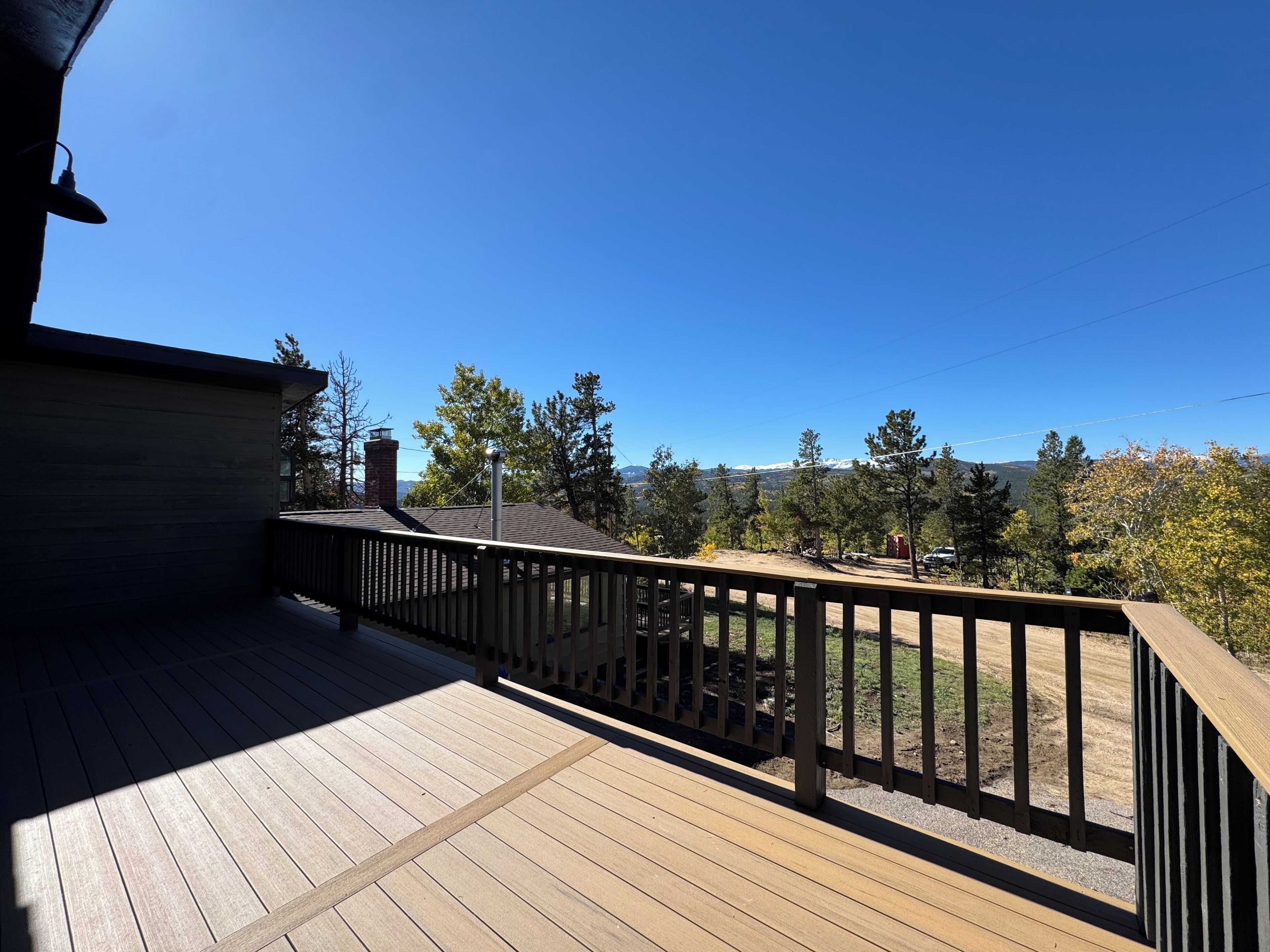 A wooden deck with a railing, overlooking a landscape with trees and a distant mountain range.