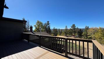 A wooden deck with a railing, overlooking a landscape with trees and a distant mountain range.