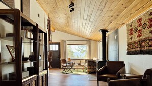 A spacious living room with a high ceiling, wooden flooring, a large fireplace, and a view of the outdoors.