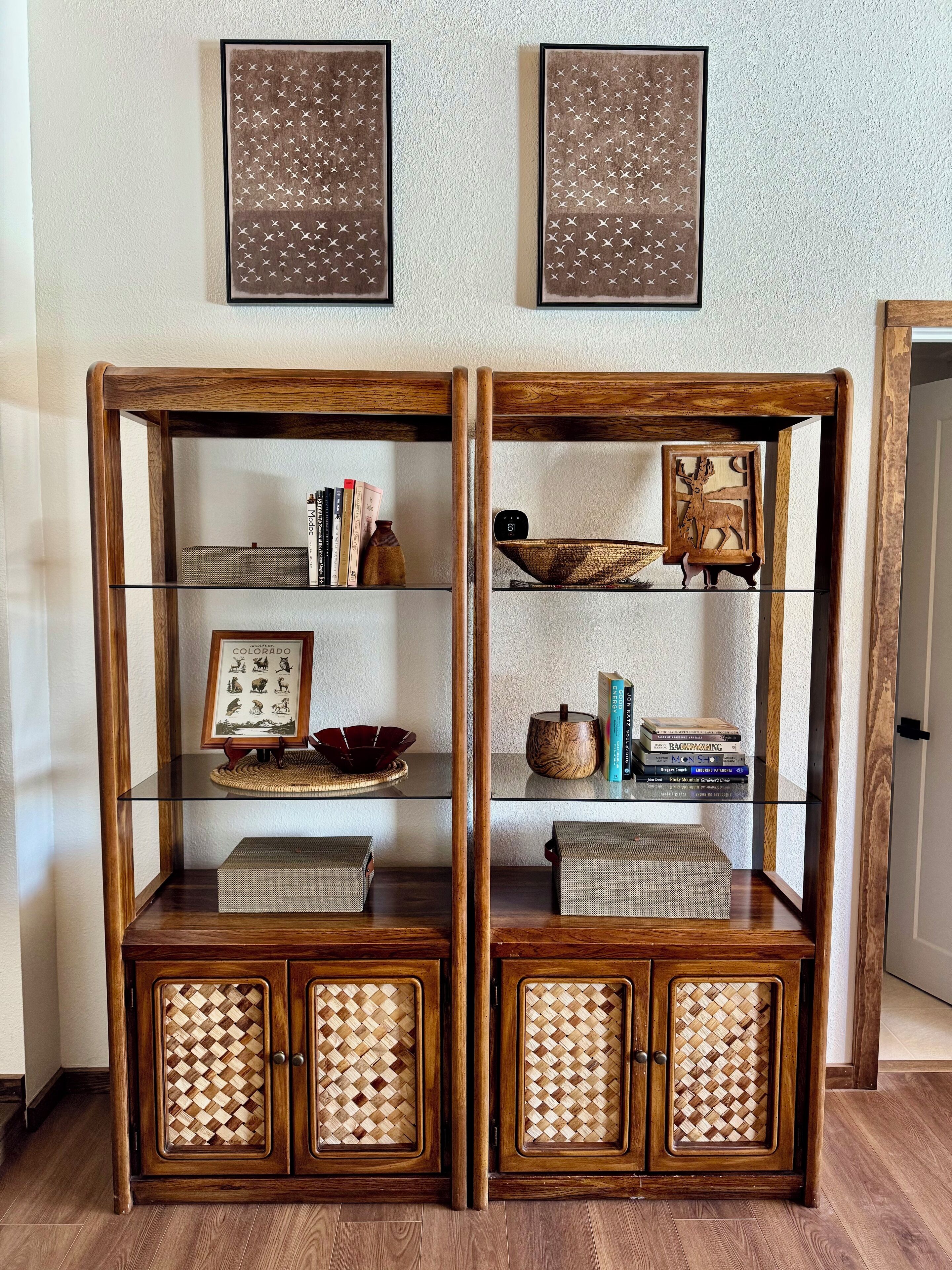 A wooden cabinet with glass shelves and woven doors, containing books, decorative items, and a framed picture.