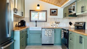 A modern kitchen with green cabinets, stainless steel appliances, and a wooden ceiling.