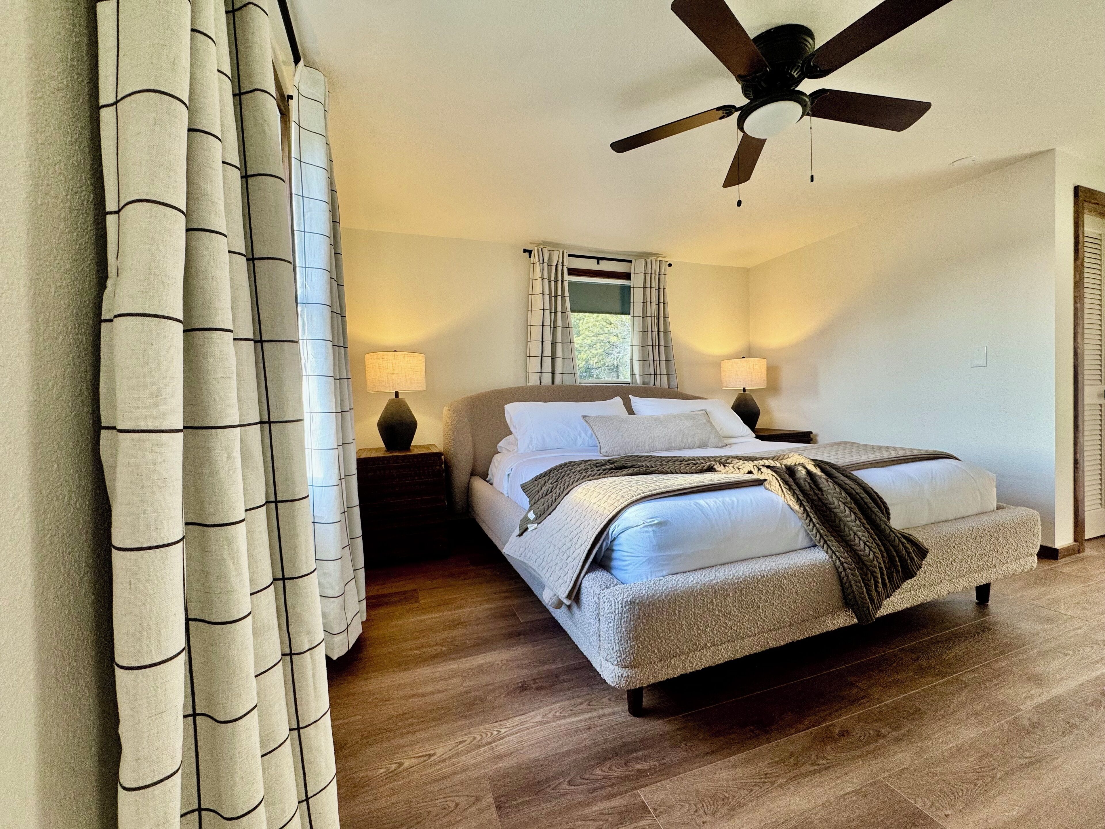 A bedroom with a bed, two bedside tables, a ceiling fan, and a window with curtains.