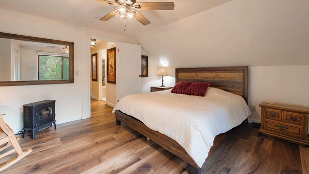Une chambre à coucher avec un lit en bois, un ventilateur de plafond, une table de chevet et une commode.