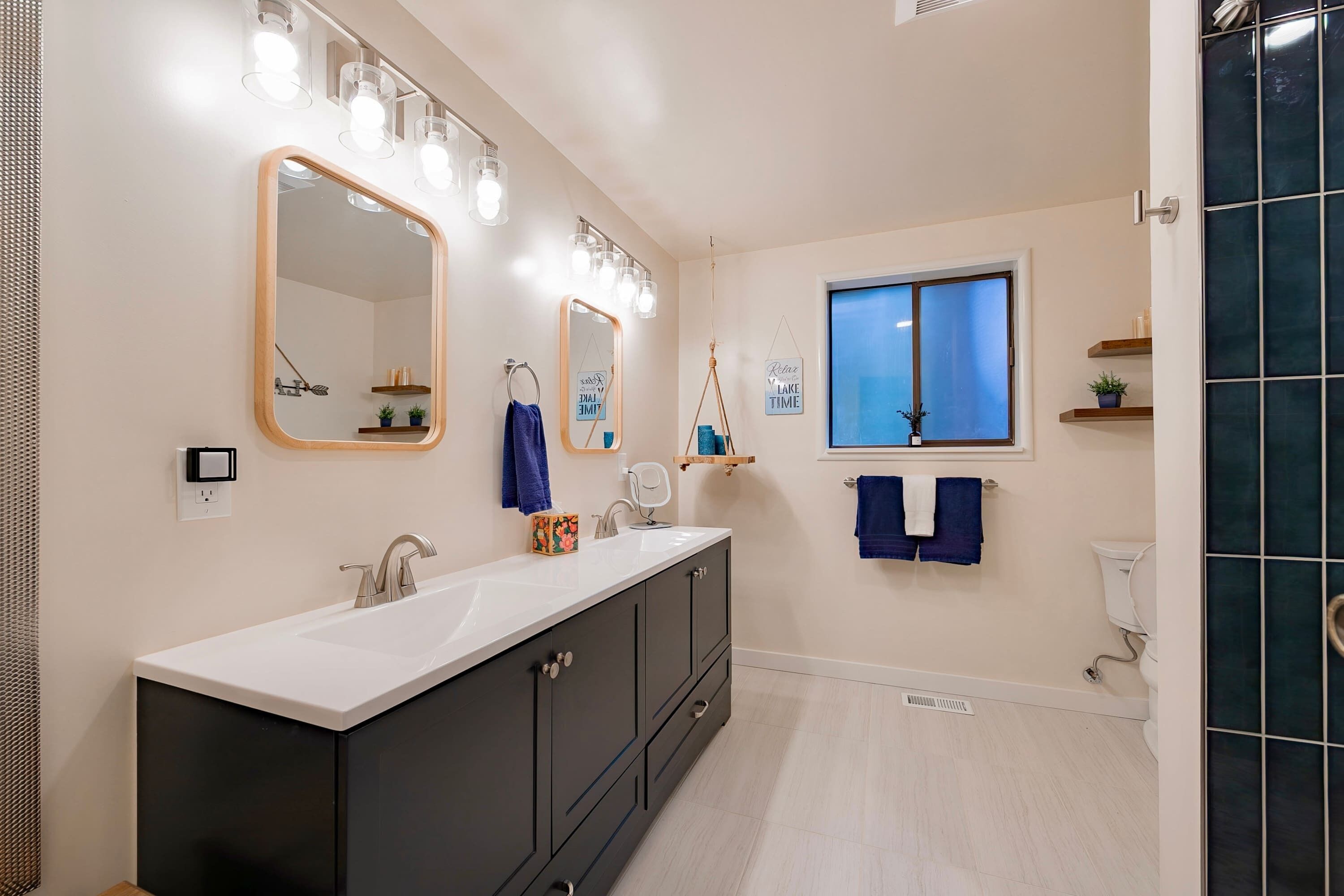 Une salle de bain moderne avec un grand miroir, deux vasques et une fenêtre.