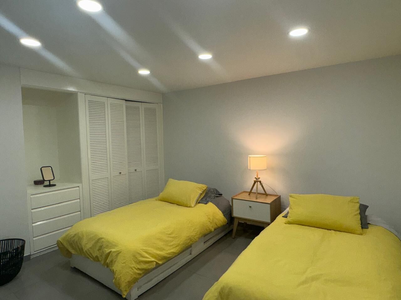 Slaapkamer met twee bedden, een nachtkastje met lamp, een kledingkast en een spiegel op een dressoir.