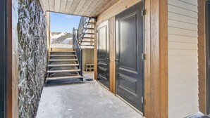 Een smalle buitenpassage met houten plafond, een stenen muur aan de zijkant, en een metalen trap die naar een deur leidt.