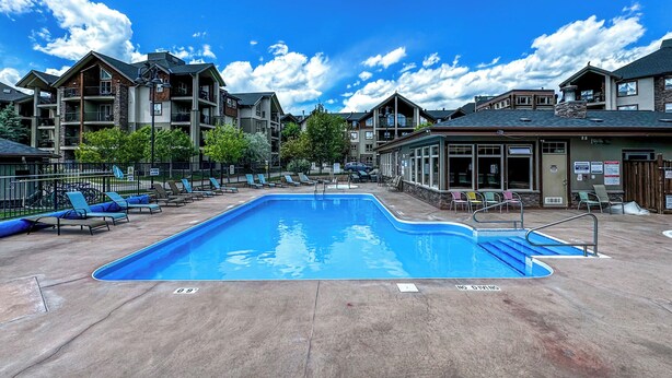 A swimming pool with lounge chairs and a building complex in the background.