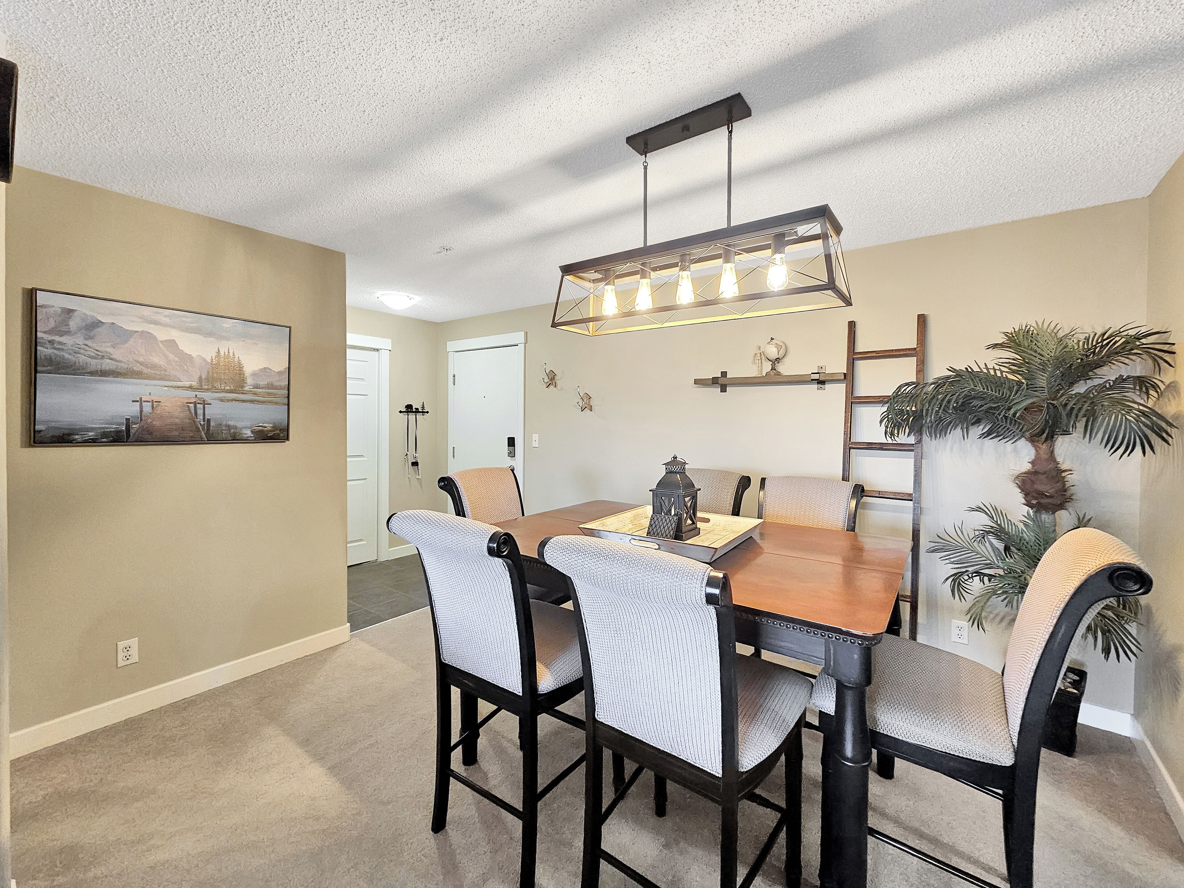 A dining area with a wooden table and chairs, a pendant light fixture, and a painting on the wall.