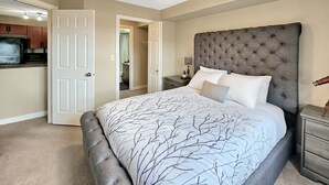 A bedroom with a tufted headboard, a bed with a tree branch pattern bedspread, a nightstand with a lamp, and a ceiling fan.