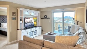 A modern living room with a sofa, a television, and a balcony with a view.