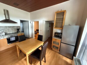 Een kleine keuken met een houten tafel, een fornuis, een magnetron en een koelkast.