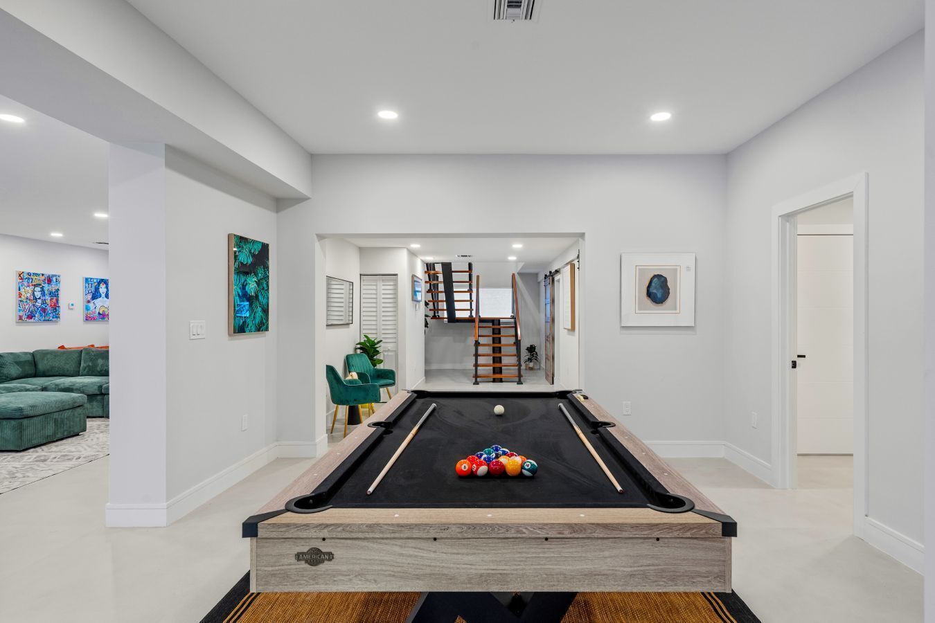 A modern living room with a pool table, a green sofa, and artwork on the walls.