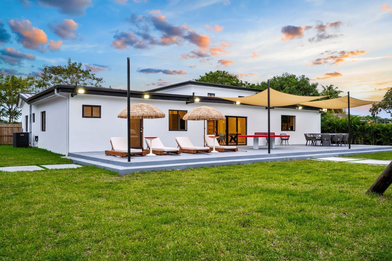 Una casa moderna con un patio que cuenta con sillones de descanso y una barbacoa.