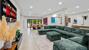 A modern living room with a sectional sofa, a dining area with a table and chairs, and a large TV displaying Netflix. - One and Only Lazy River Pool Villa (North Miami)