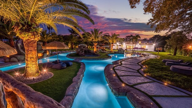 A swimming pool with a winding design, surrounded by stone pathways and palm trees. - One and Only Lazy River Pool Villa (North Miami)