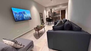 A modern living room with a flat-screen TV mounted on the wall, a grey sofa with patterned cushions, and a small wooden coffee table with decorative items. - Awesome Location @ Dana - Arboleda in San Pedro (San Pedro Garza García)