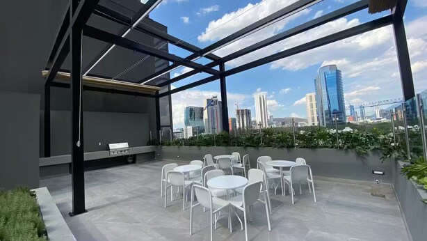 A rooftop terrace with white chairs and tables, a glass enclosure, and a city skyline view. - Awesome Location @ Dana - Arboleda in San Pedro (San Pedro Garza García)