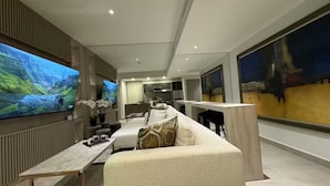 Uma sala de estar moderna com uma grande televisão de tela plana, um sofá, uma mesa de centro e uma área de jantar.