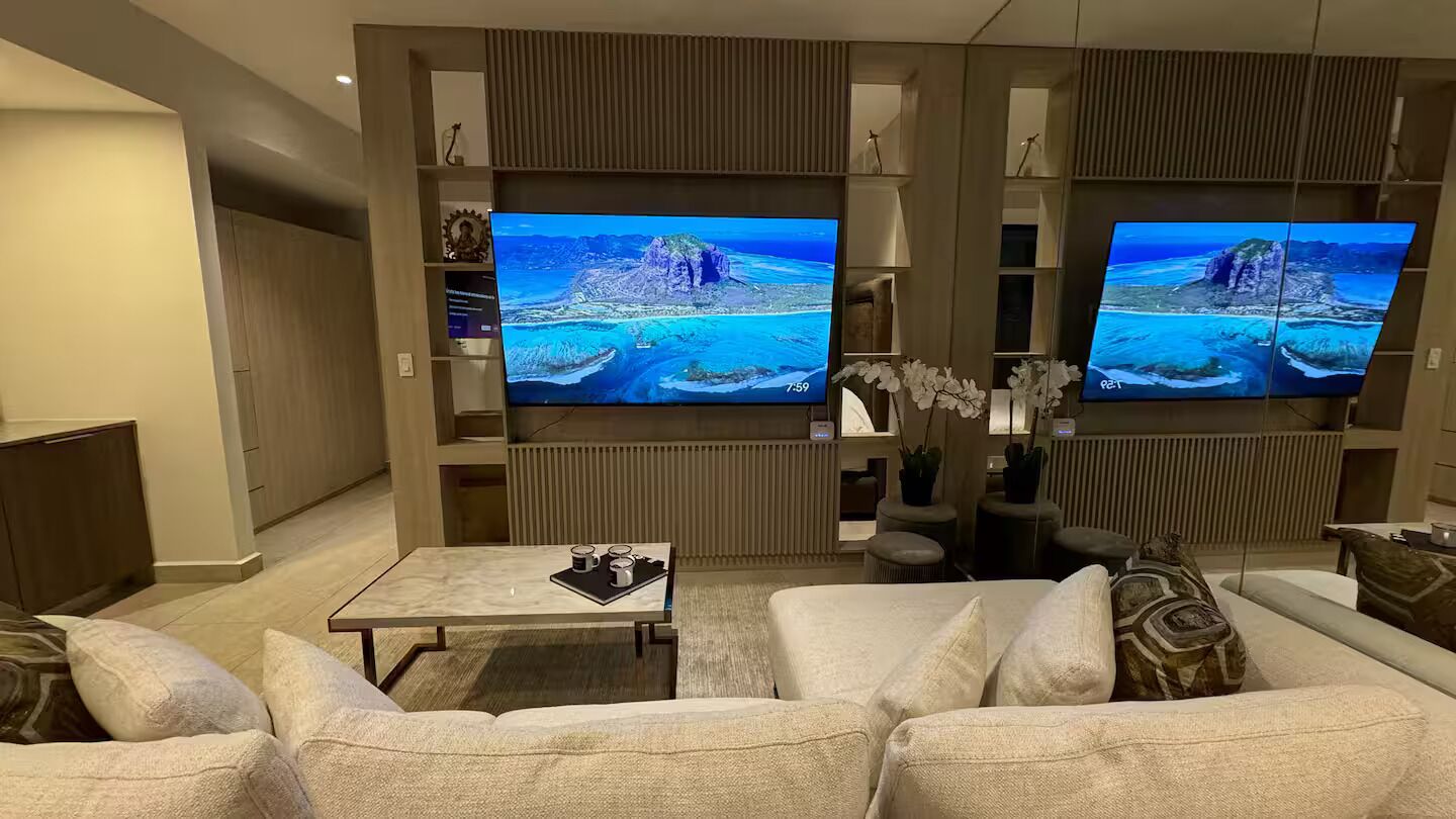 Un salon moderne doté d’un grand téléviseur à écran plat, d’un canapé, d’une table basse et d’une plante décorative.