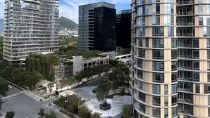 Uma área urbana moderna com edifícios altos, uma rotatória central e vegetação ao redor.