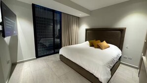 Quarto de hotel moderno com uma cama grande, televisão de tela plana e vista para a cidade pela janela.