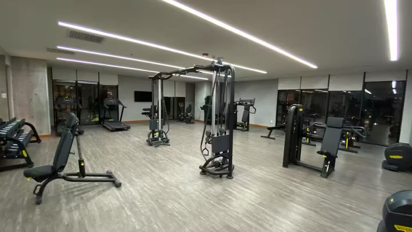 Ein modernes Fitnessstudio mit unterschiedlichen Trainingsgeräten, großen Fenstern und einer sauberen, übersichtlichen Gestaltung.