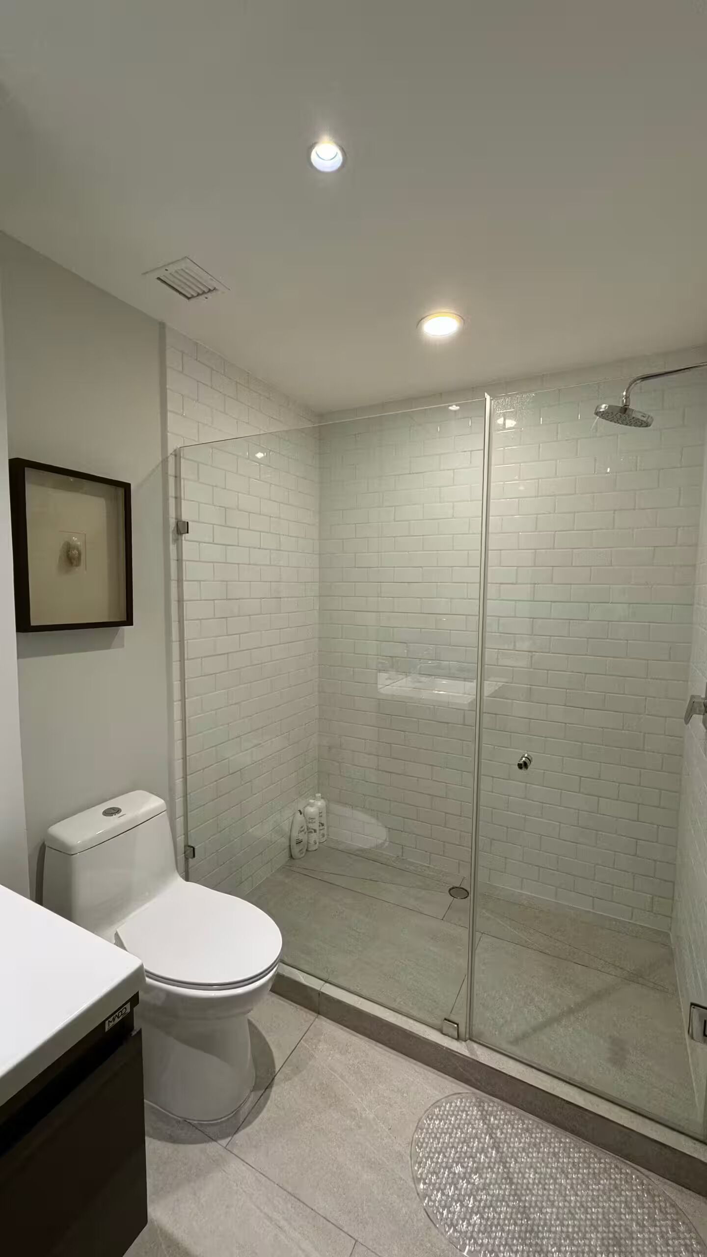 Uma casa de banho moderna com cabine de duche em vidro, paredes revestidas a azulejo branco, sanita e lavatório.