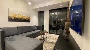 Una sala moderna con un sofá gris, una mesita redonda con plantas, una bicicleta decorativa y un cuadro abstracto grande en la pared.