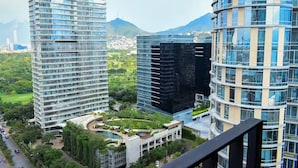 Un edificio moderno de gran altura con fachada de vidrio, rodeado de abundante vegetación y una vista despejada de una montaña al fondo.