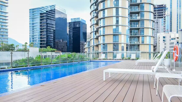 Una piscina en la azotea con sillones de descanso y un flotador salvavidas, rodeada de modernos edificios de gran altura.