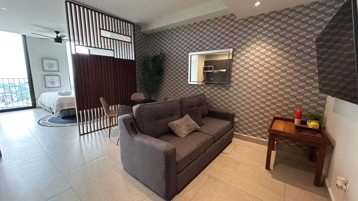 A modern living room with a grey sofa, a wooden coffee table, and a patterned wall.