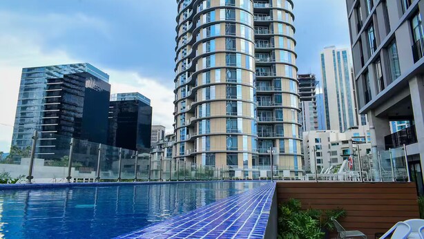 Un immeuble moderne de grande hauteur, doté d’une façade incurvée et d’une piscine en premier plan.