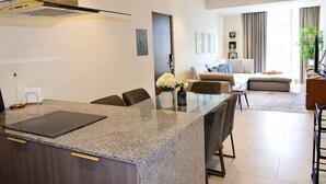 Une cuisine moderne avec des comptoirs en granit, un coin repas doté d’une table en verre et un salon avec un canapé et une table basse.